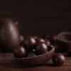 Barra de chocolate amargo quebrada em pedaços com amêndoas e ovos de Páscoa artesanais ao fundo, representando opções de chocolate saudável.
