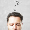 Ilustração conceitual da cabeça de um homem com símbolos de sono "zzzzz" saindo de sua mente sobre um fundo cinza, representando o cansaço no inverno e a sonolência.